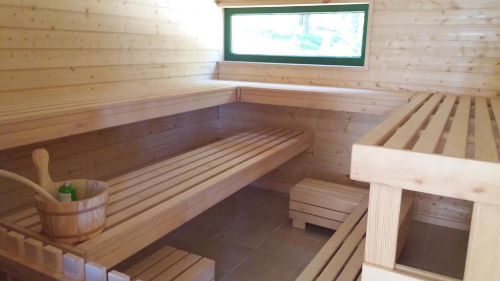 Wood-paneled sauna with tiered benches, wooden ladle bucket and narrow exterior window.