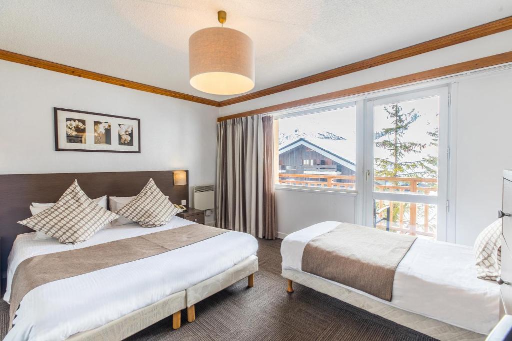 a bedroom with two beds and a large window at Madame Vacances Hôtel & Spa Le Mottaret in Méribel