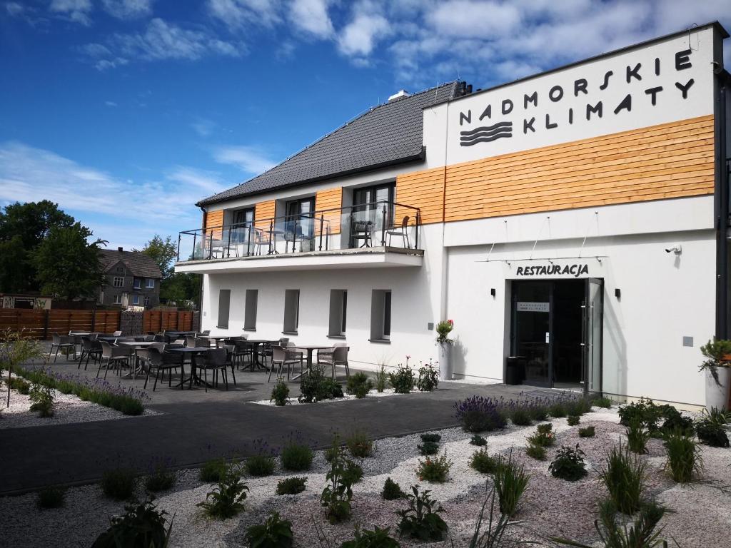 a white building with a balcony and tables and chairs at Nadmorskie Klimaty in Sarbinowo