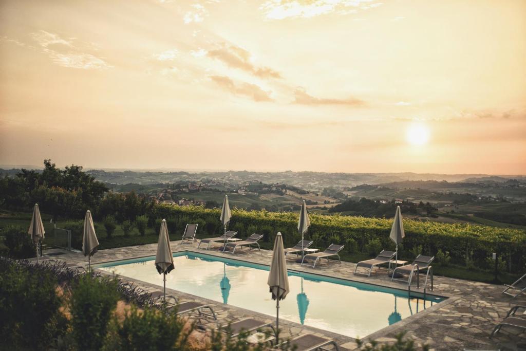 una piscina con sombrillas y sillas y una puesta de sol en La Cascina Della Musica, en Costigliole dʼAsti