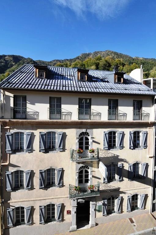 - un grand bâtiment blanc avec des fenêtres et un toit dans l'établissement Hôtel La Montagne Fleurie, à Barèges