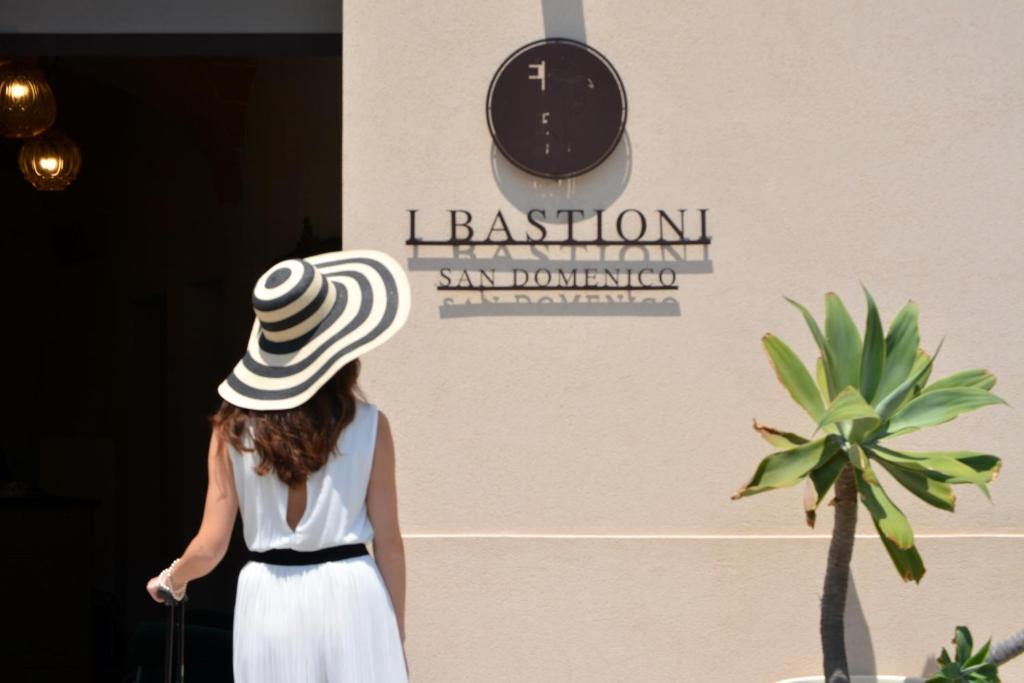 Una donna con un cappello che cammina oltre un muro con un orologio di I Bastioni San Domenico - Boutique Hotel a Gallipoli