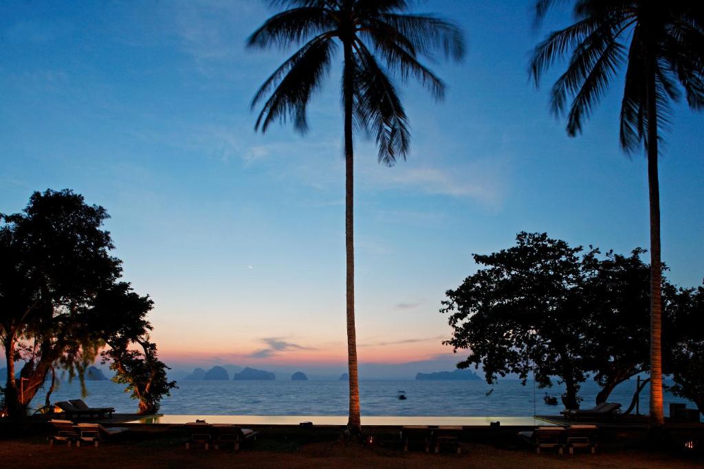 two palm trees and benches on the beach at sunset at Koyao Island Resort in Ko Yao Noi