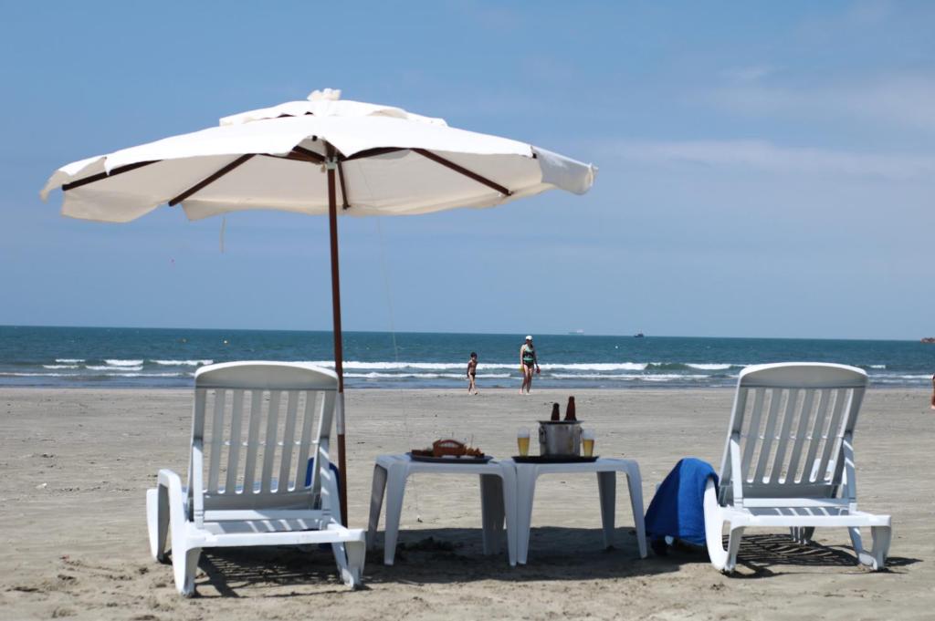 duas cadeiras e uma mesa debaixo de um guarda-sol na praia em Pris Hotel em Barequeçaba