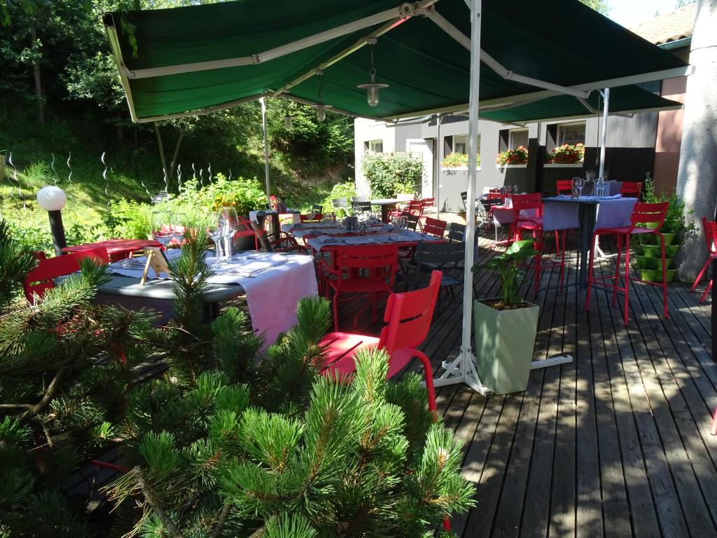 um pátio com mesas e cadeiras sob um guarda-sol verde em Logis Hotel Restaurant La Tour em Dunières
