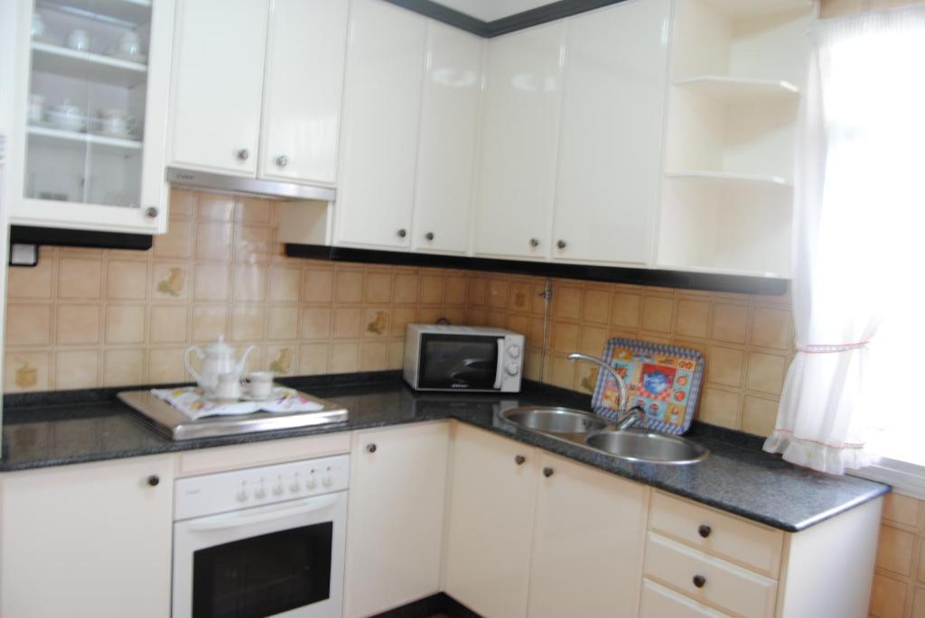 a kitchen with white cabinets and a sink and a microwave at Casa La Torre in Isla de Arosa