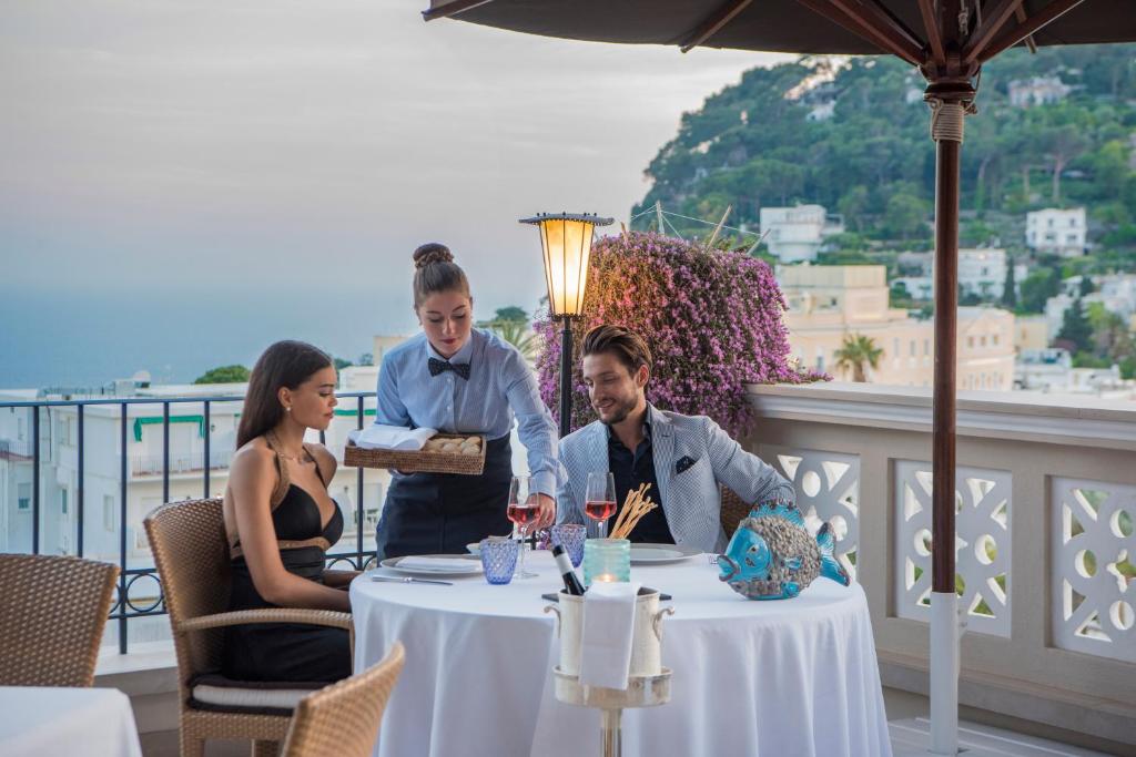 a man and woman sitting at a table with wine glasses at Capri Tiberio Palace - The Leading Hotels of the World in Capri