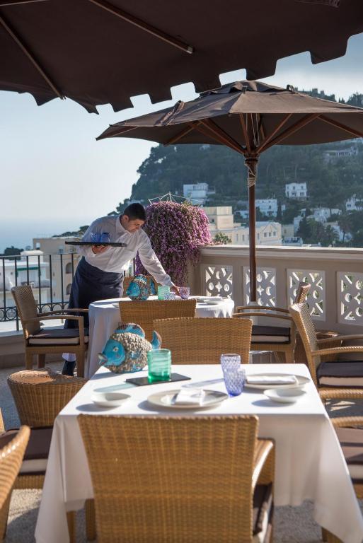 a woman standing on a patio with tables and an umbrella at Capri Tiberio Palace - The Leading Hotels of the World in Capri