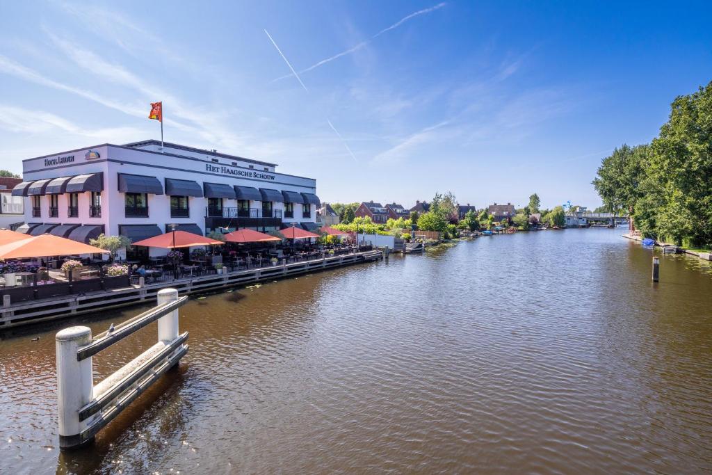 einen Fluss mit einem Gebäude mit Tischen und Sonnenschirmen in der Unterkunft Van der Valk Hotel Leiden in Leiden