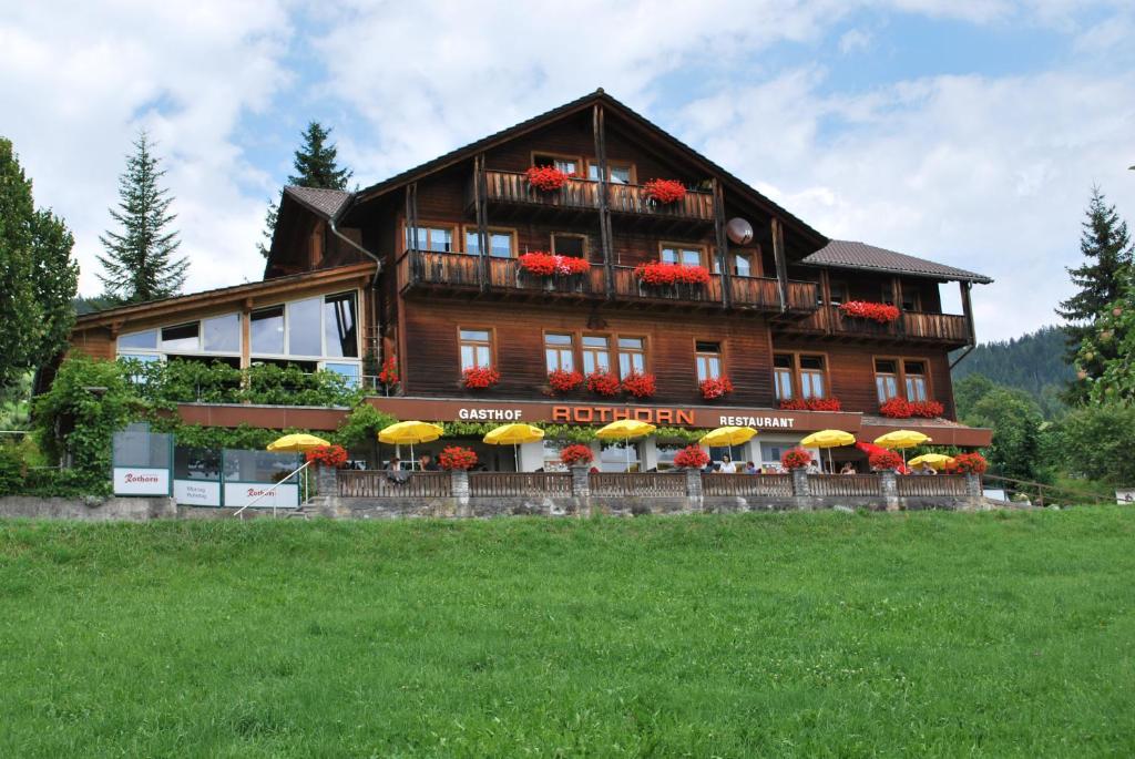 ein großes Holzhaus mit Sonnenschirmen davor in der Unterkunft Hotel Rothorn in Schwanden