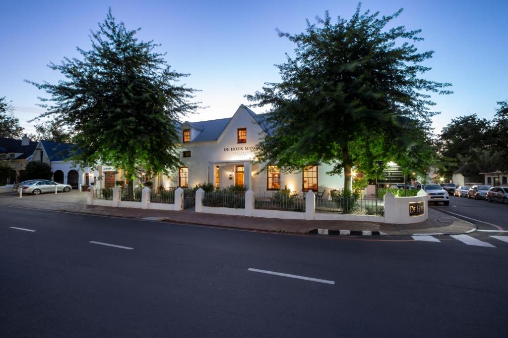 a white house with trees on the side of a street at De Hoek Manor in Stellenbosch