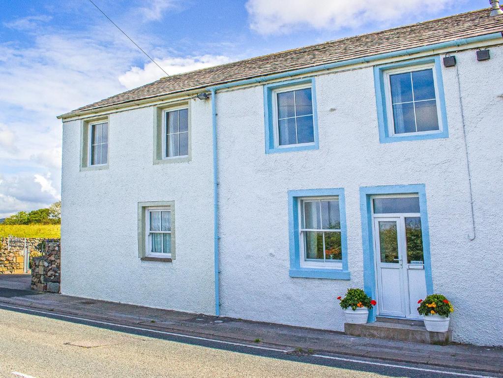 a white house with blue windows on a street at 2 Park Nook Close in Waberthwaite