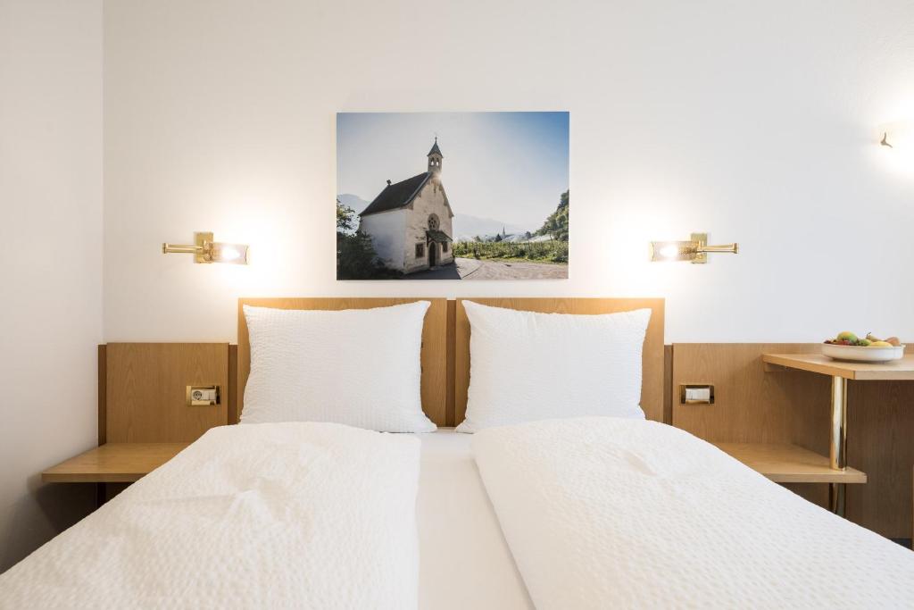 a bed with white sheets and a picture of a church at Mondschein Rooms in Lana
