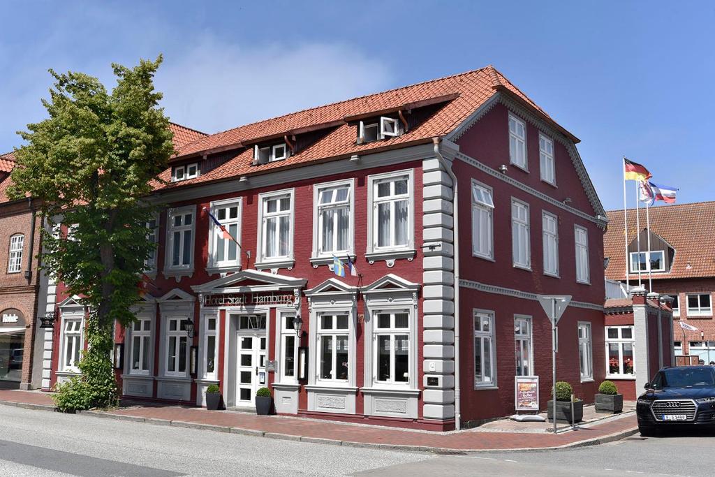 een rood-wit gebouw met een auto ervoor geparkeerd bij Hotel Stadt Hamburg in Heiligenhafen