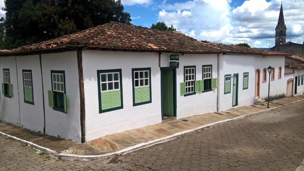 a white building with green shutters on a street at Pousada do Ipe in Goiás