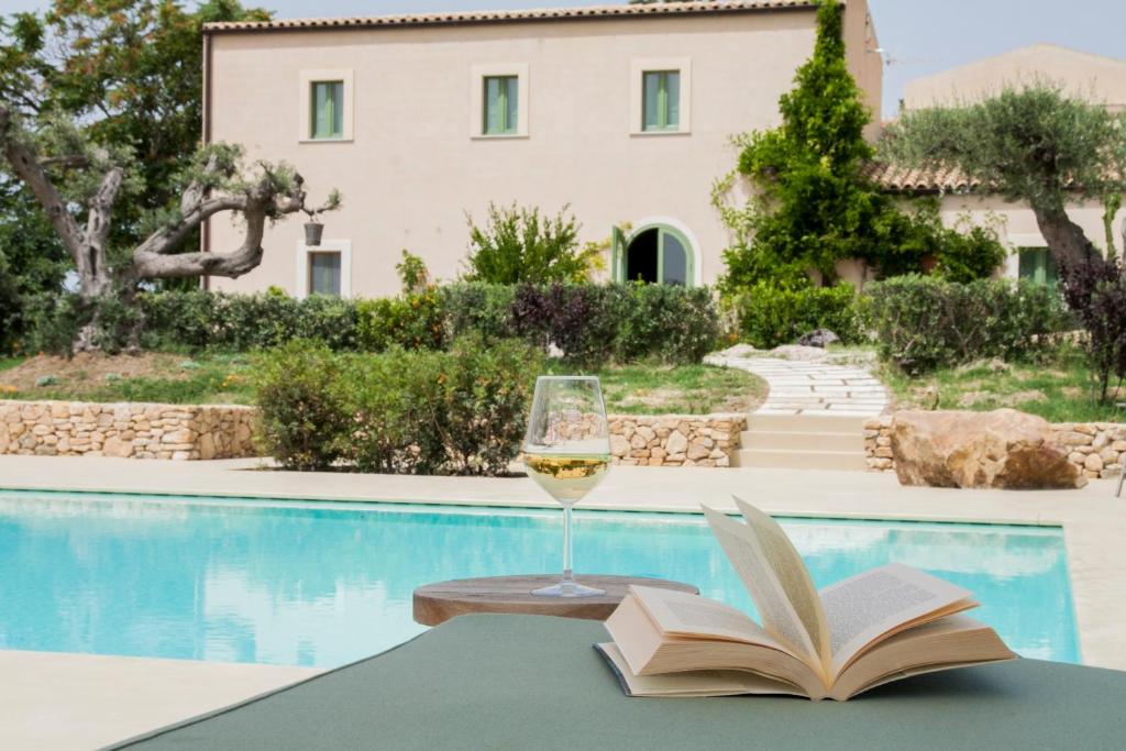 un bicchiere di vino e un libro su un tavolo accanto alla piscina di Resort Fontes Episcopi ad Aragona