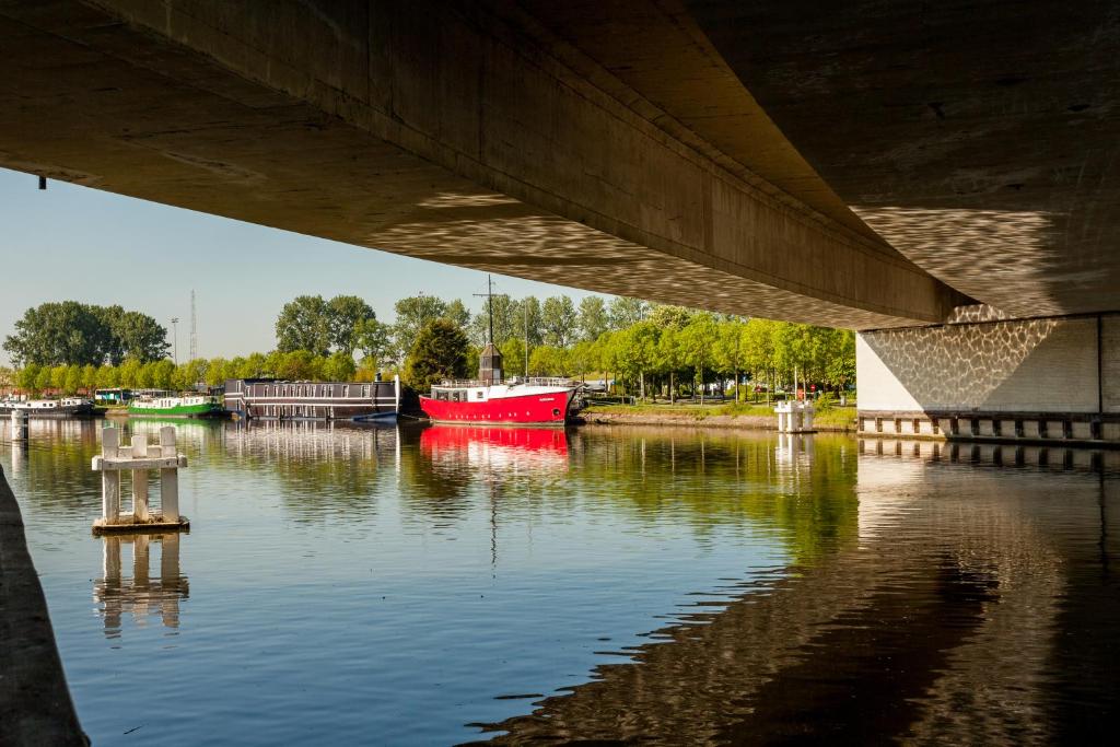 a red boat on the water under a bridge at Boat Hotel De Barge in Bruges