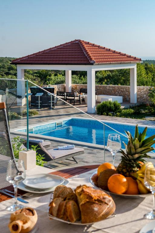 a table with bread and fruit on it next to a swimming pool at Villa Daly in Primošten