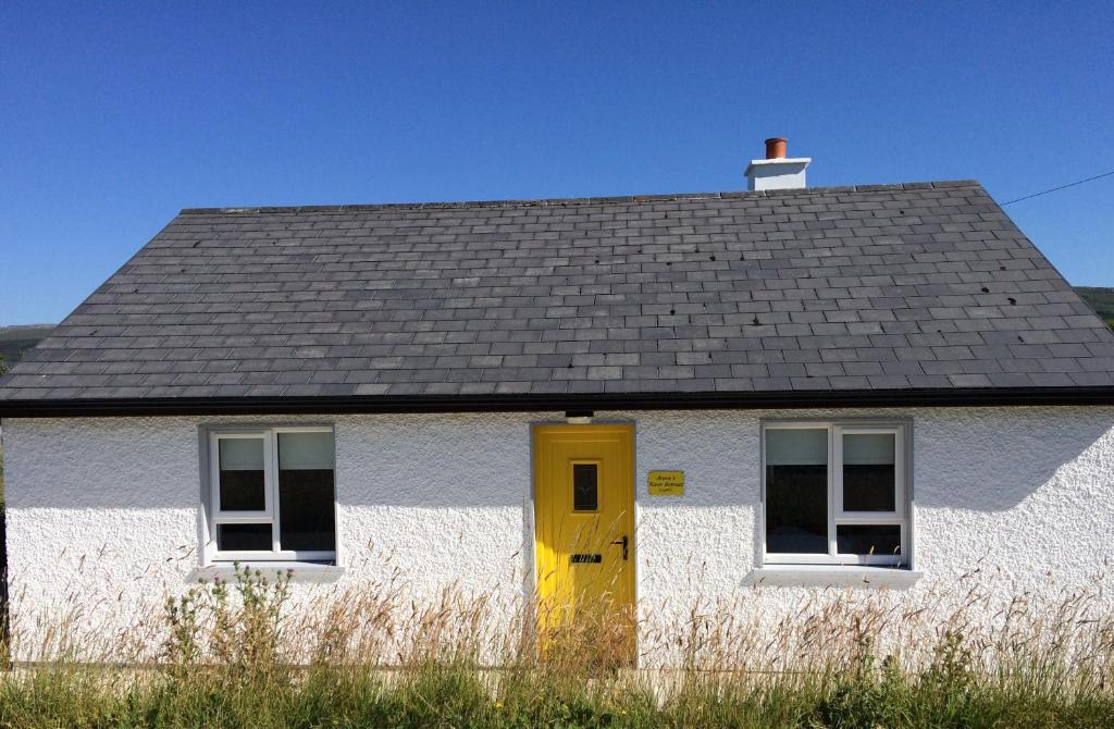 a white house with a yellow door and a roof at Annie's River Retreat in Doochary