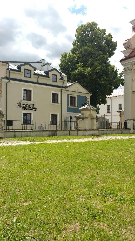 a large white house with a fence and a grass field at Hostel Starówka in Zamość