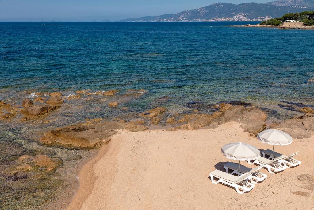 two lounge chairs on a beach near the water at Hotel Le Maquis in Porticcio