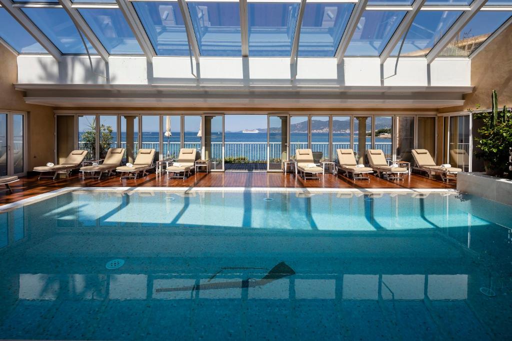 a swimming pool with chairs and the ocean in the background at Hotel Le Maquis in Porticcio