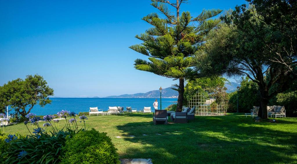 a person standing in a yard with a tree and the ocean at Hotel Le Maquis in Porticcio