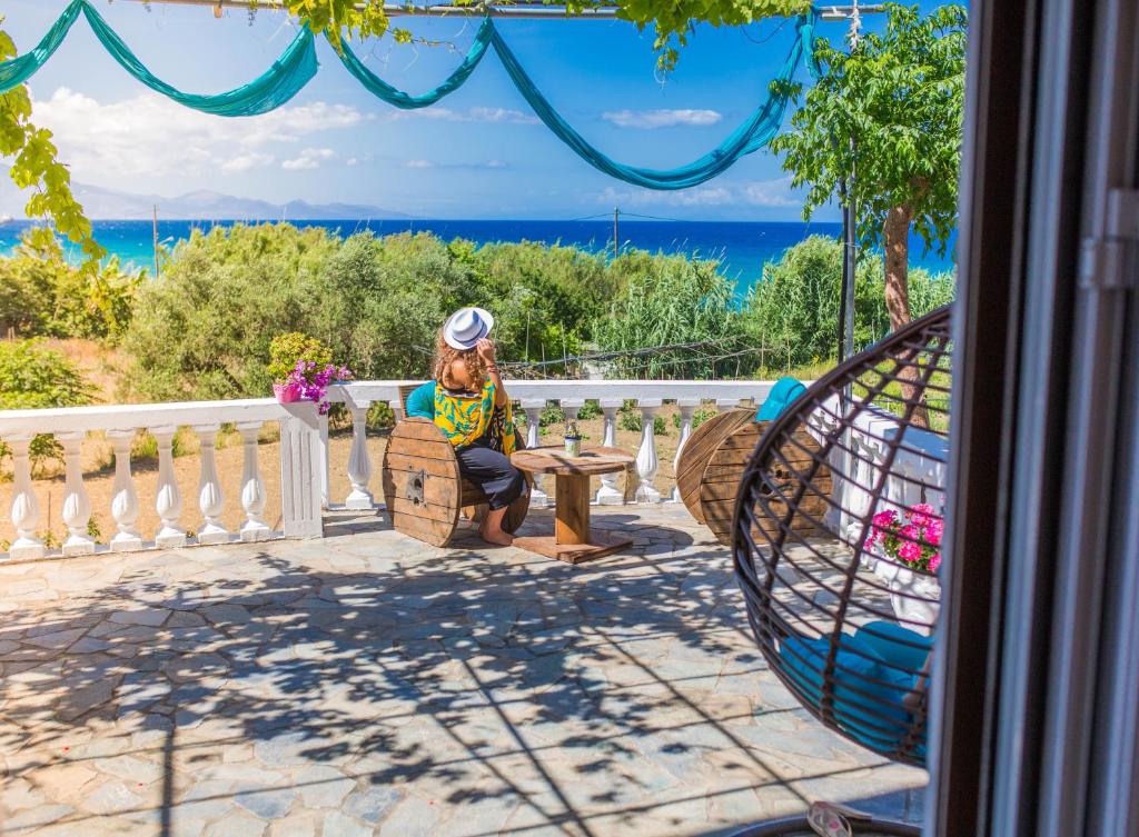 a woman sitting on a bench on a balcony overlooking the ocean at Ammos Apartments in Alikanas