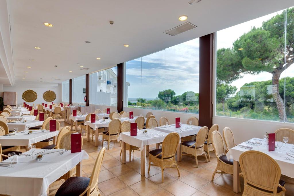 a restaurant with white tables and chairs and a large window at Garden Playanatural - Adults Only in El Rompido
