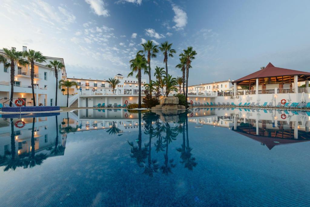 a large swimming pool with palm trees and buildings at Garden Playanatural - Adults Only in El Rompido