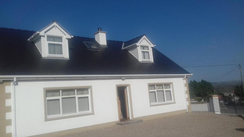 een wit huis met twee ramen en een zwart dak bij Teach Nellie Cottage in Loughanure