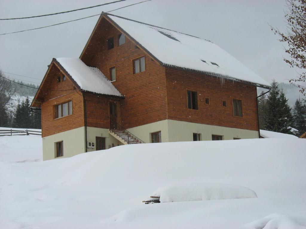 a house with a snow covered roof in front of it at Pensiunea Aries in Arieşeni