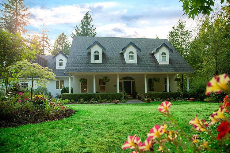 a white house with a green yard with flowers at The Inlet Bed & Breakfast in Saanichton