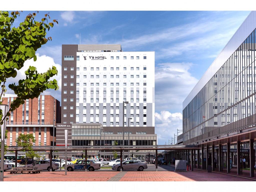 un edificio blanco alto con coches estacionados frente a él en Y's Hotel Asahikawa Ekimae en Asahikawa