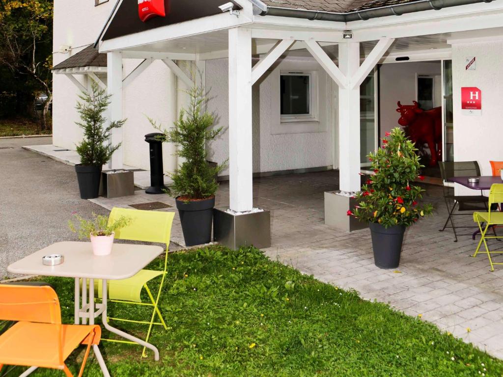 un patio avec des chaises, des tables et des plantes en pot dans l'établissement ibis Dole Sud Choisey, à Choisey