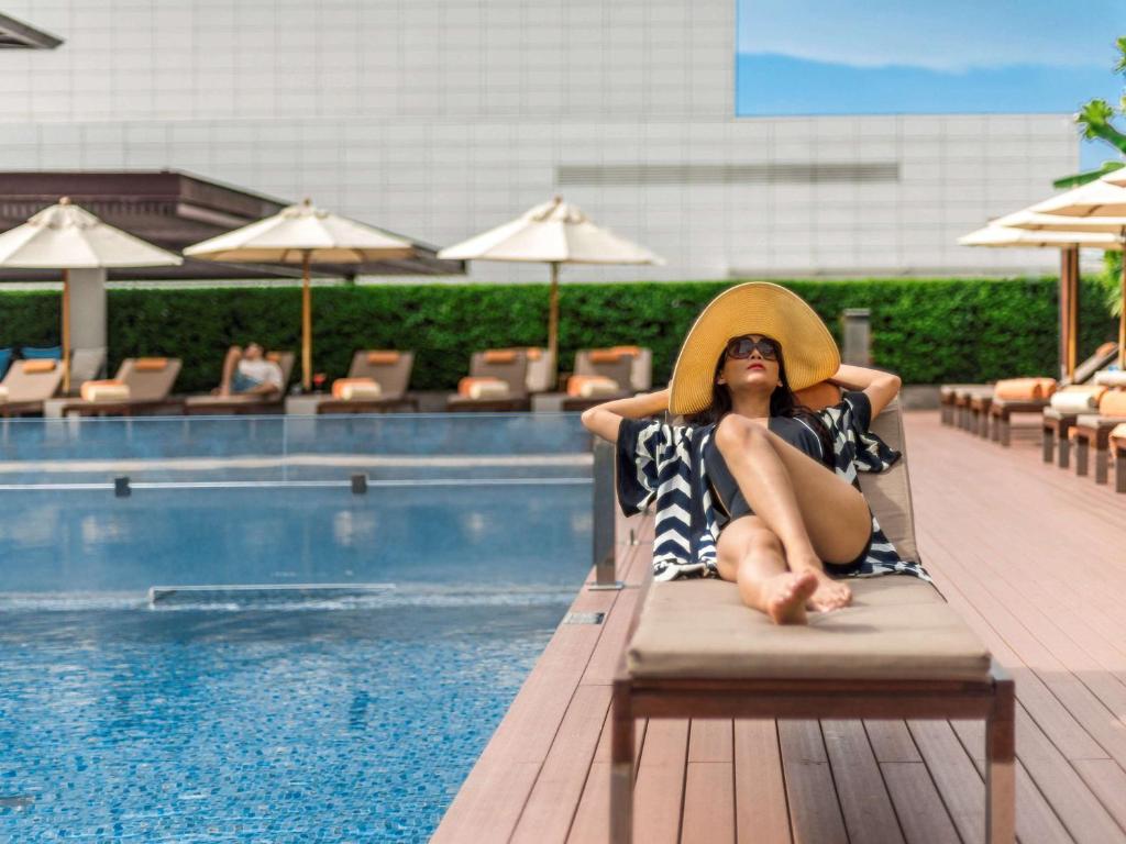 a woman in a hat sitting in a chair next to a pool at Pullman Bangkok King Power in Bangkok