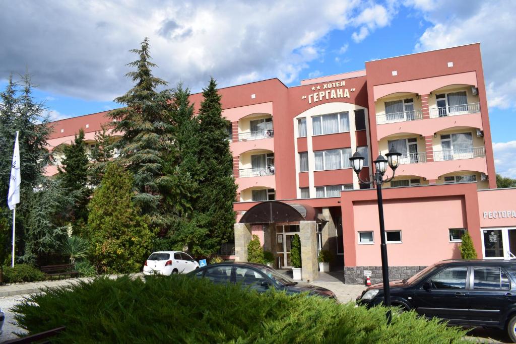 a pink hotel with cars parked in a parking lot at Балнеохотел "Гергана" in Hisarya
