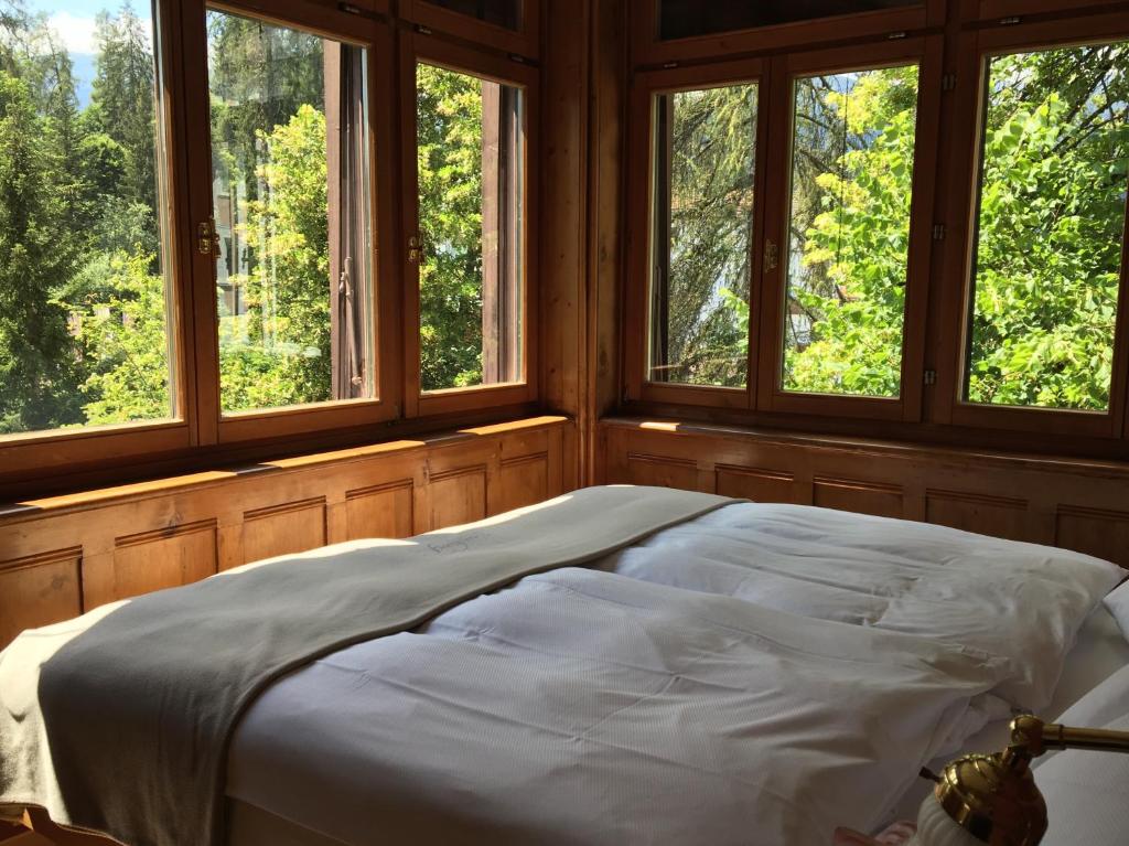 Bett in einem Zimmer mit 3 Fenstern in der Unterkunft Stilvolle 3-Zimmer Wohnung in Jugendstilvilla in Flims