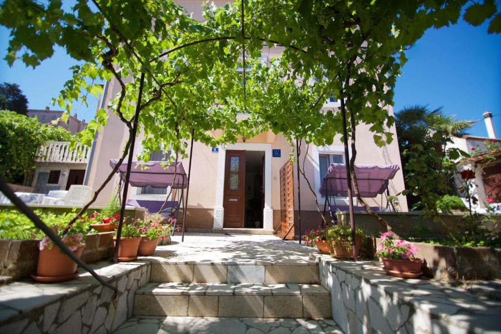 a house with a porch with trees and potted plants at Apartmani Loreta in Mali Lošinj