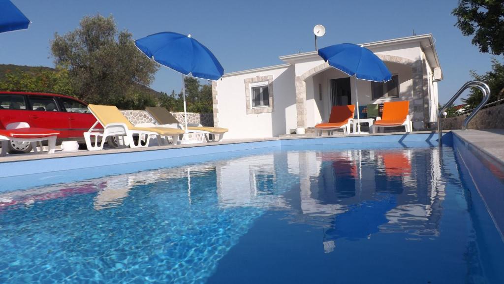 a pool with chairs and umbrellas next to a house at Vila Rogač in Tivat