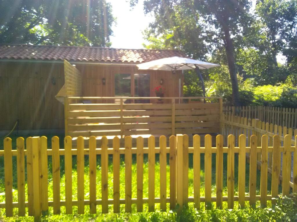 a wooden cabin with an umbrella behind a fence at La Grange et Le Nid in Biscarrosse