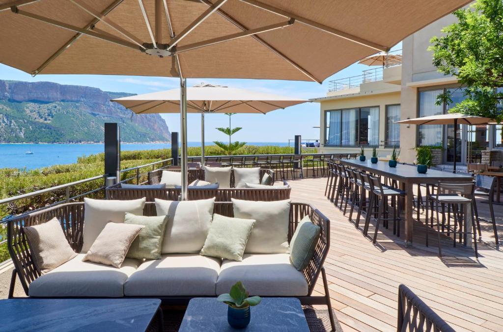 a patio with a couch and tables and umbrellas at Hôtel Les Roches Blanches Cassis in Cassis