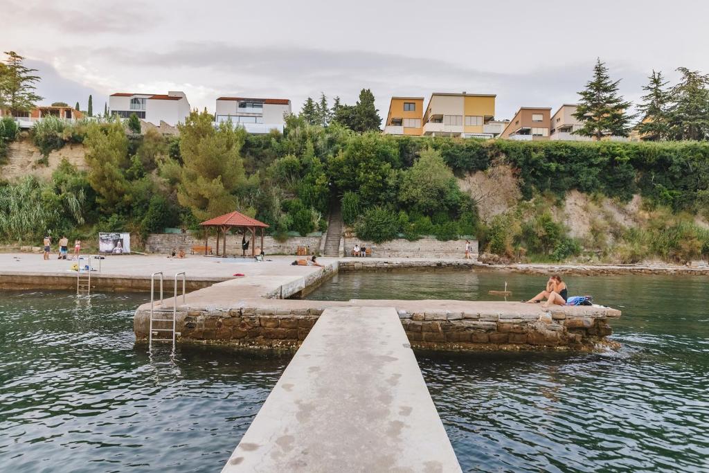 a woman sitting on a dock in a body of water at Apartma Joy - private beach in Ankaran