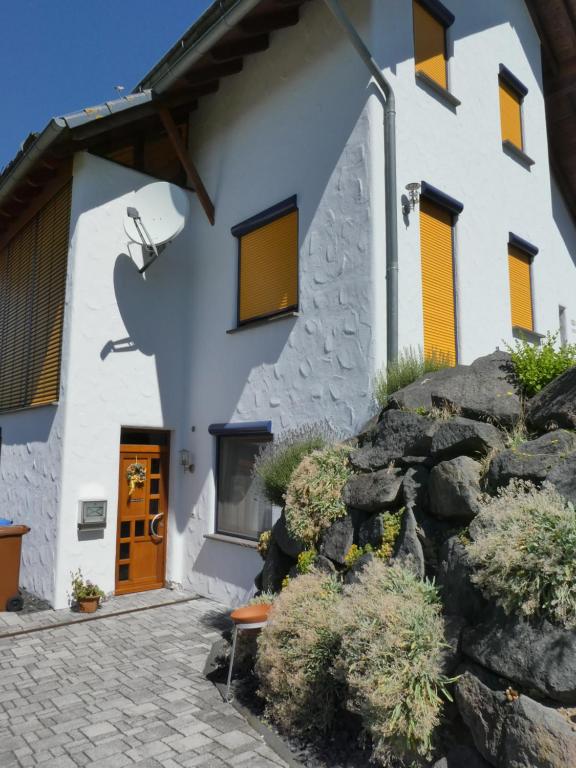 a white building with yellow windows and a stone wall at Ferienwohnung am Klosterweg Rhein-Westerwald in Kurtscheid