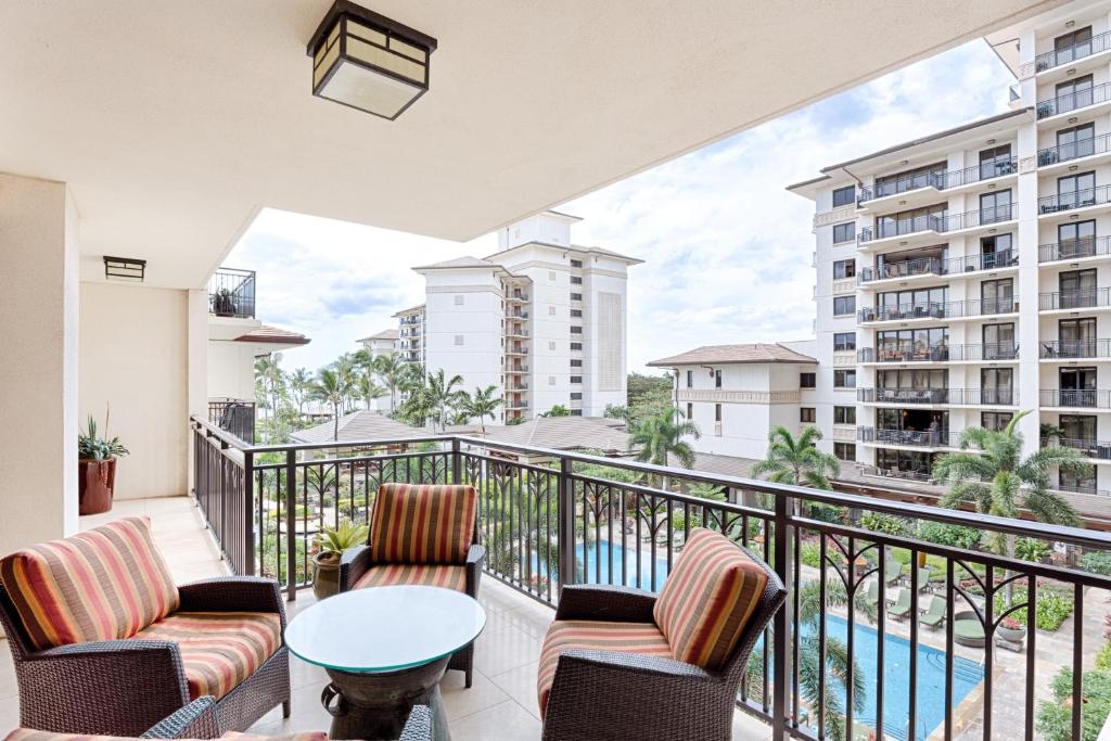 a balcony with chairs and a table and a pool at Spacious Fourth Floor Villa with Pool View - Ocean Tower at Ko Olina Beach Villas Resort in Kapolei