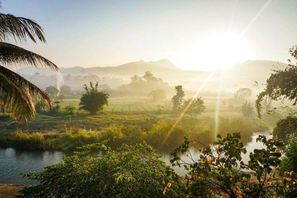 a misty sunrise over a river in a field at UP2U Guesthouse in Pai