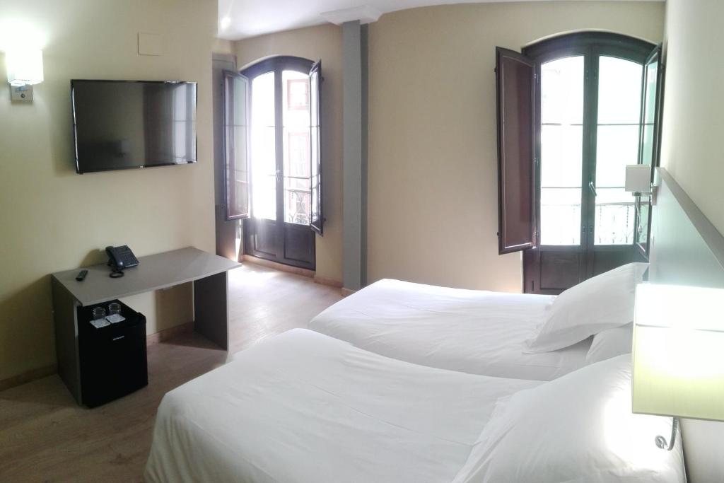 a hotel room with two beds and a desk and two windows at Hotel Areces in Grado