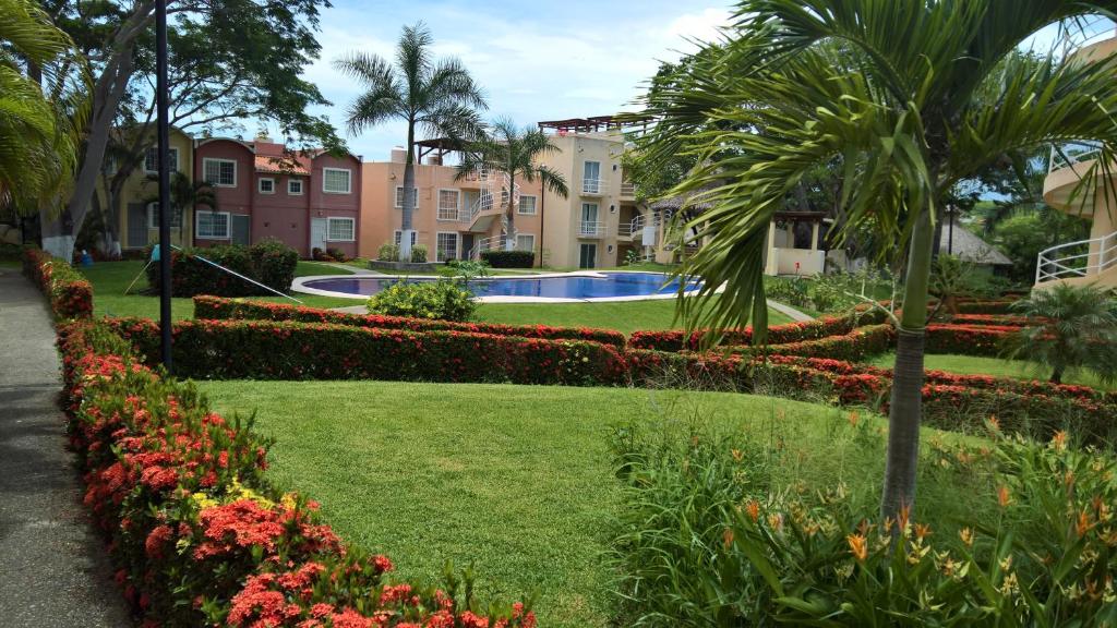 a park with flowers and palm trees and buildings at Casa Flamingos 25 in Ixtapa