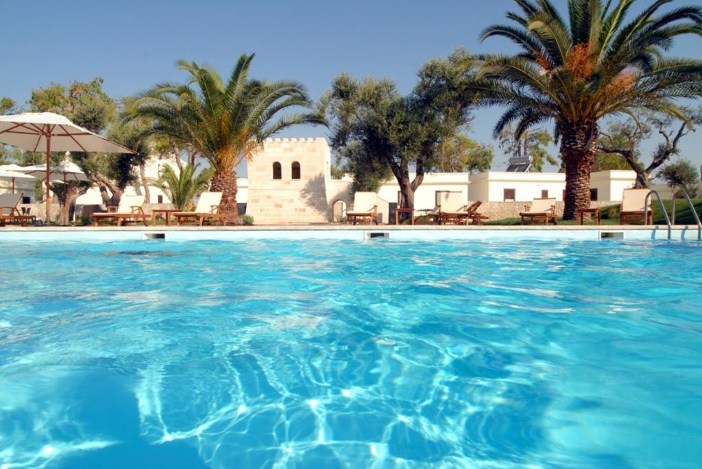 a swimming pool with palm trees and a building at Resort Villa Hermosa in Porto Cesareo