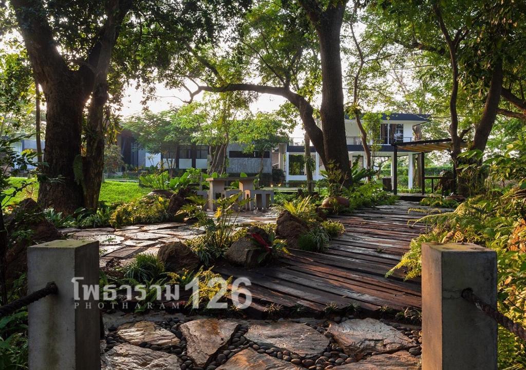 een houten loopbrug in een tuin met bomen bij Photharam126 Resort in Ban Khlong Ta Khot